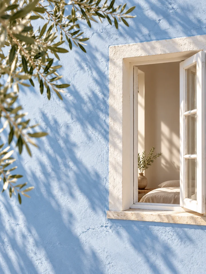 Ventana blanca abierta en una pared azul con luz y sombras de vegetación