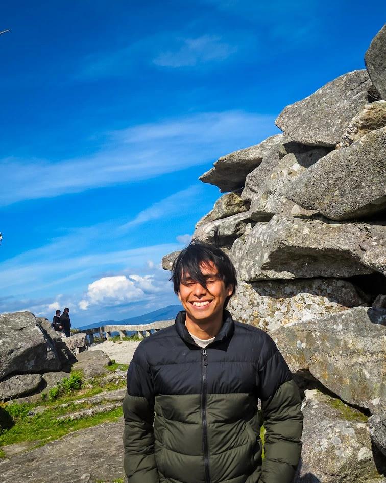 Luis sonriendo al aire libre, junto a unas rocas bajo el cielo azul